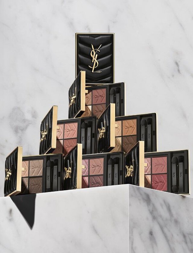 A stylish display of Yves Saint Laurent makeup palettes stacked in a pyramid formation on a marble surface, with a sleek black case at the top.