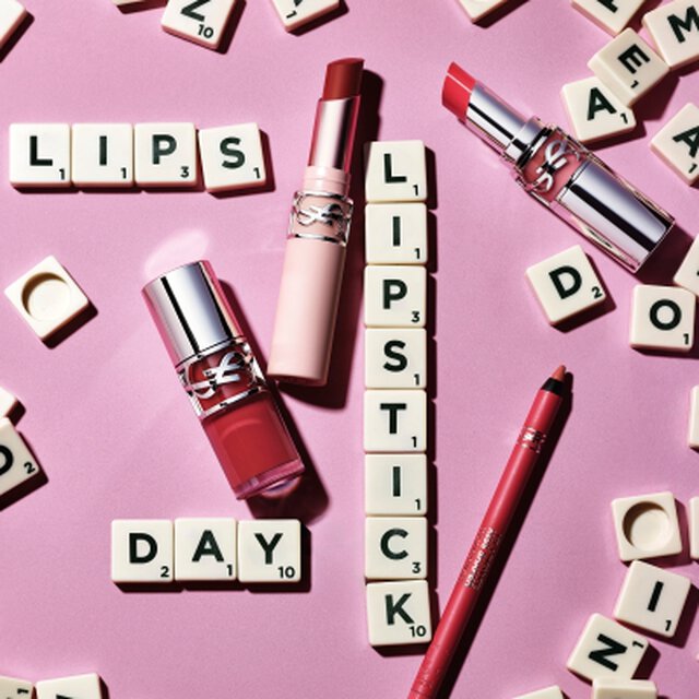 YSL lippenstiften en lippotlood op een roze achtergrond met Scrabble-letters die de woorden "LIPS", "LIPSTICK" en "DAY" vormen