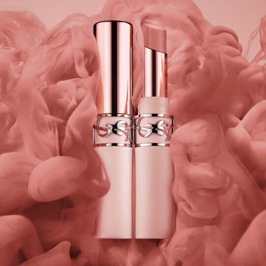 Twee rosegouden lipsticks tegen een zachte roze rokerige achtergrond.