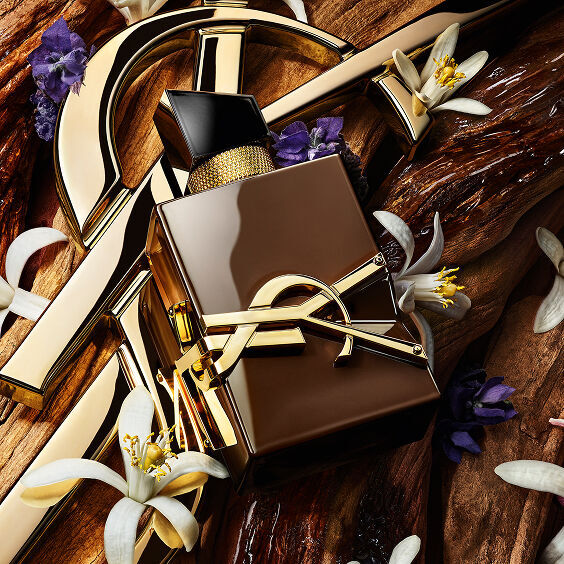 YSL Libre parfumflacon omringd door gouden accenten, witte oranjebloesem en paarse bloemen op een houten achtergrond.