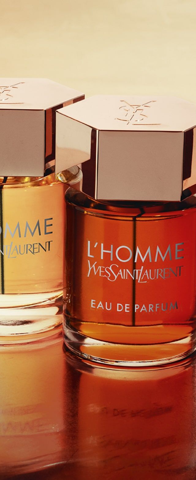 Vier flessen parfum van Yves Saint Laurent, elk met een hexagonale dop en stijlvolle etiketten, staan op een glanzend houten oppervlak.