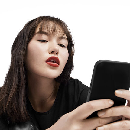 Een vrouw met lange, donkerbrune haren en rode lippen kijkt naar haar smartphone.