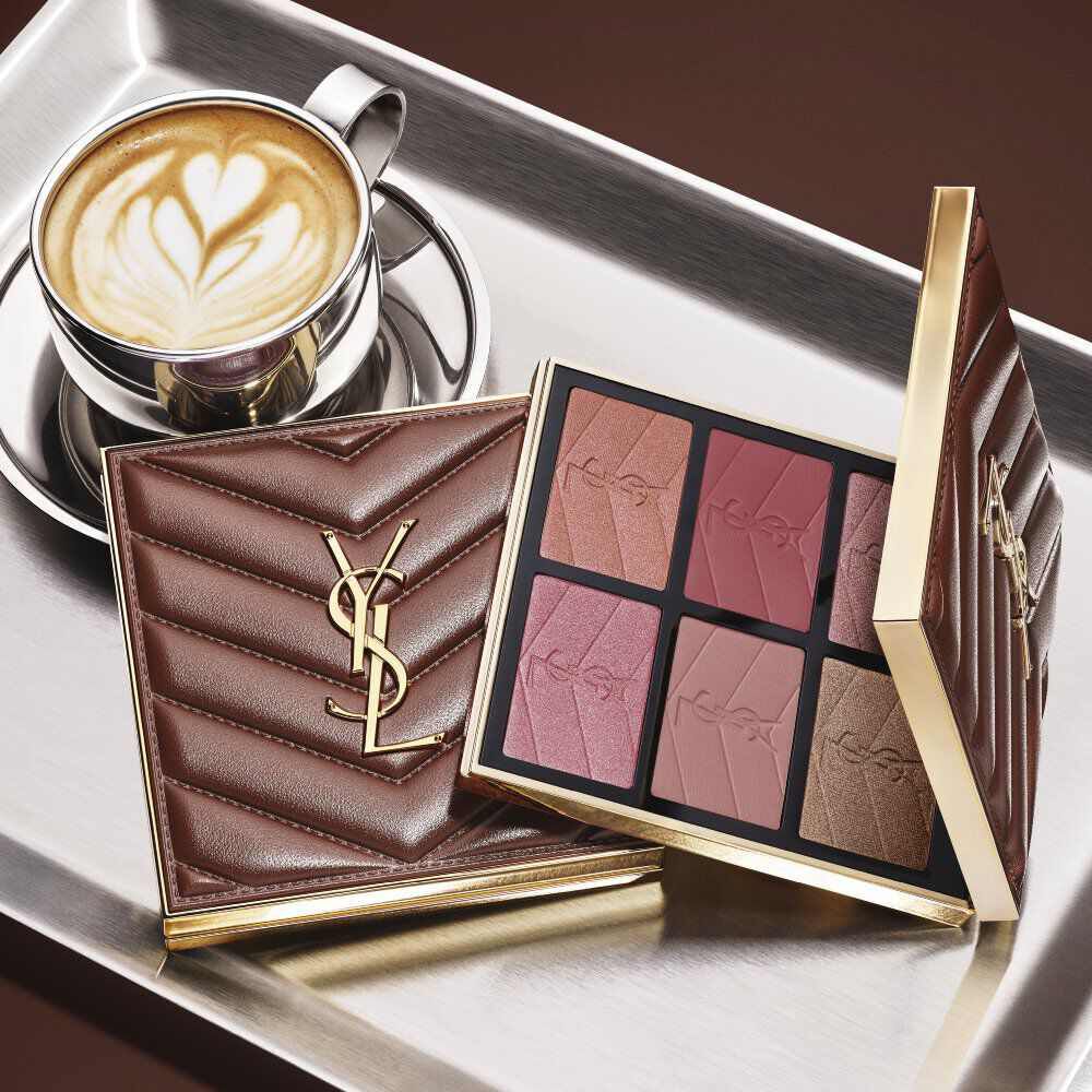 YSL-make-uppalet en doorgestikte clutch naast een kop koffie op een zilveren dienblad.