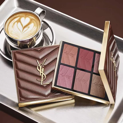 YSL-make-uppalet en doorgestikte clutch naast een kop koffie op een zilveren dienblad.