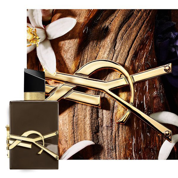 Libre Santal Couture geglazuurde bruine flacon op sandelhoutschors met gouden Cassandre en witte bloemen.