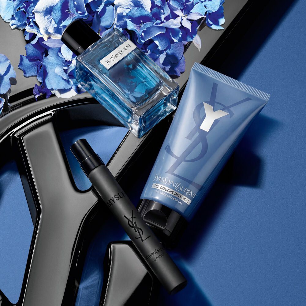 YSL-geur, reisspray en douchegel op een blauwe bloemige achtergrond.