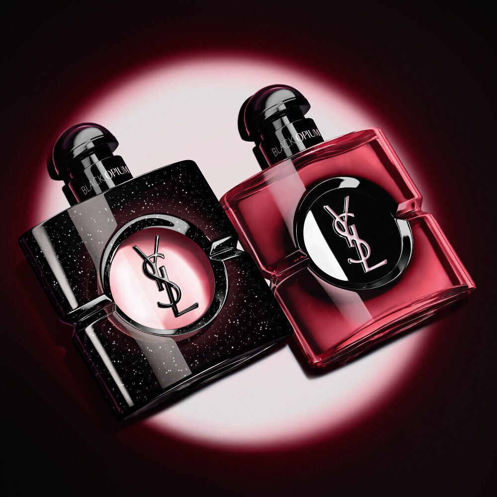 Twee verlichte Yves Saint Laurent Black Opium parfumflacons tegen een donkere achtergrond.