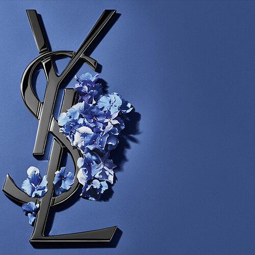Een groot, glinsterend roze glitterhart op een zachtroze achtergrond. Het iconische gouden Yves Saint Laurent (YSL) monogramlogo is elegant verticaal over het hart geplaatst.
