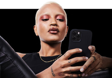 Een persoon met kort, lichtblond haar en opvallende make-up houdt een smartphone vast, terwijl ze recht in de camera kijkt.