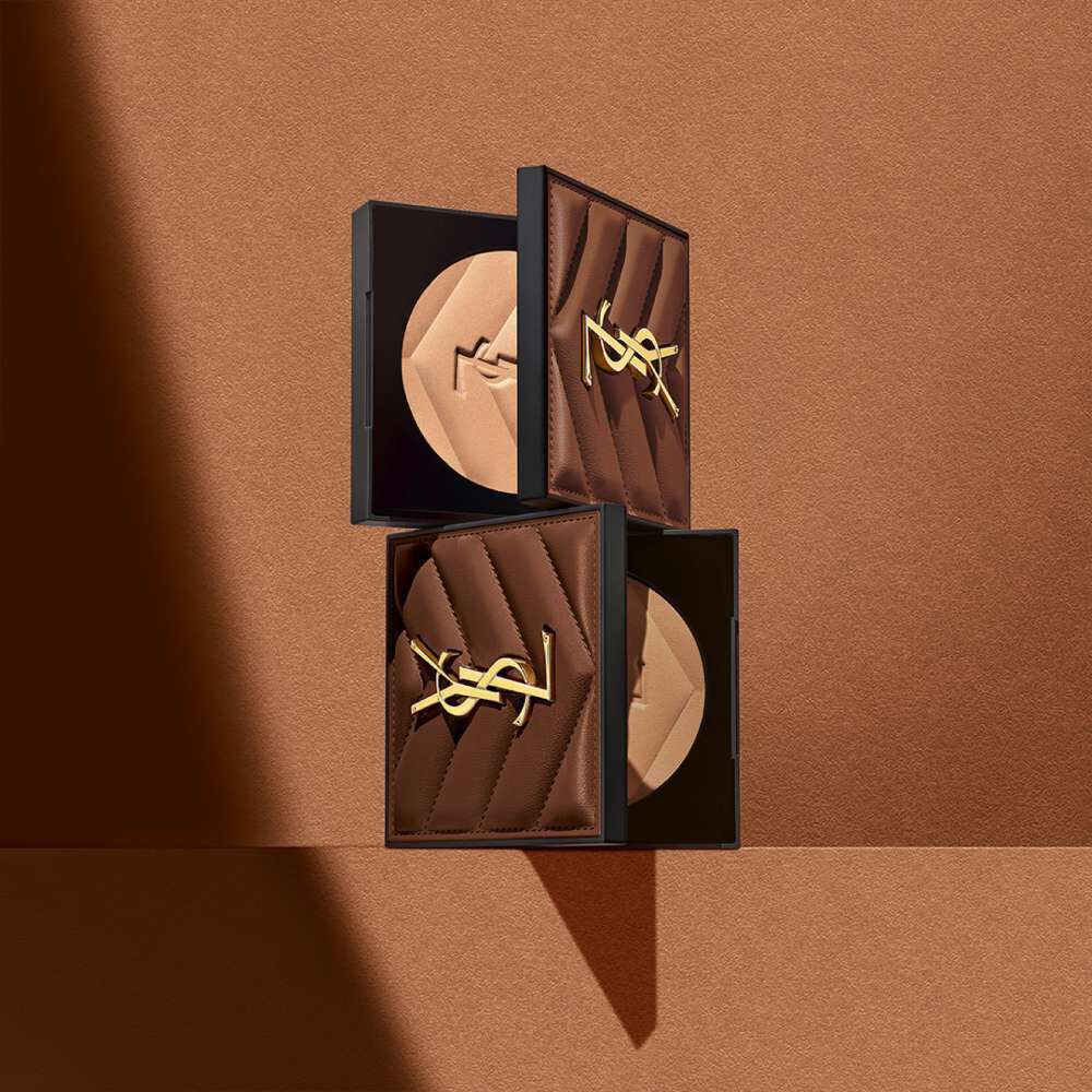 Three elegant makeup compacts with a quilted design and a gold logo, arranged against a warm brown background.