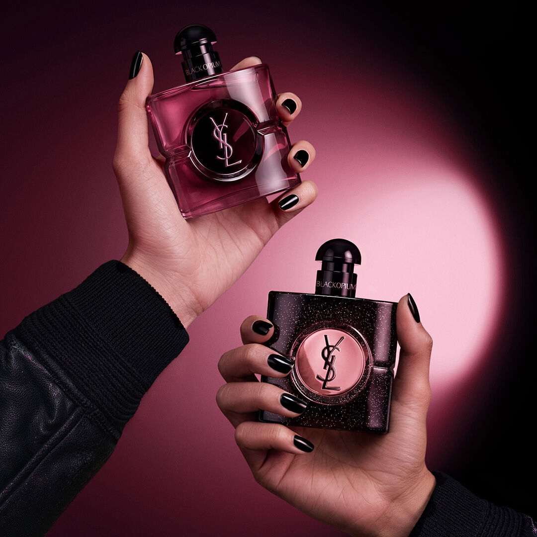 Twee YSL Black Opium-flacons op roze achtergrond met bloemen en koffiebonen