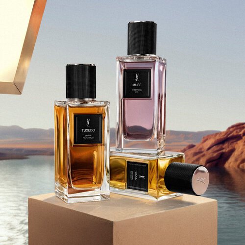 Flacons van YSL Le Vestiaire des Parfums op een sokkel bij een woestijnmeer.