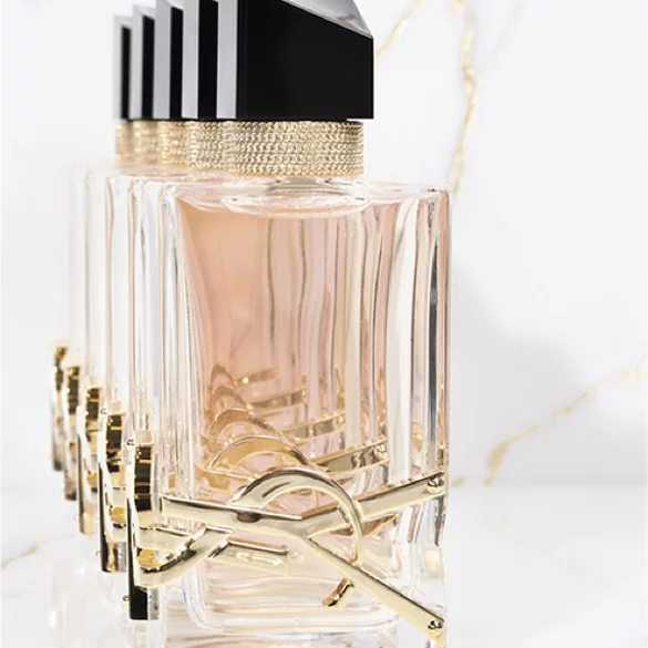 A row of elegant perfume bottles with clear glass bodies, gold accents, and black lids, arranged against a light marble background.
