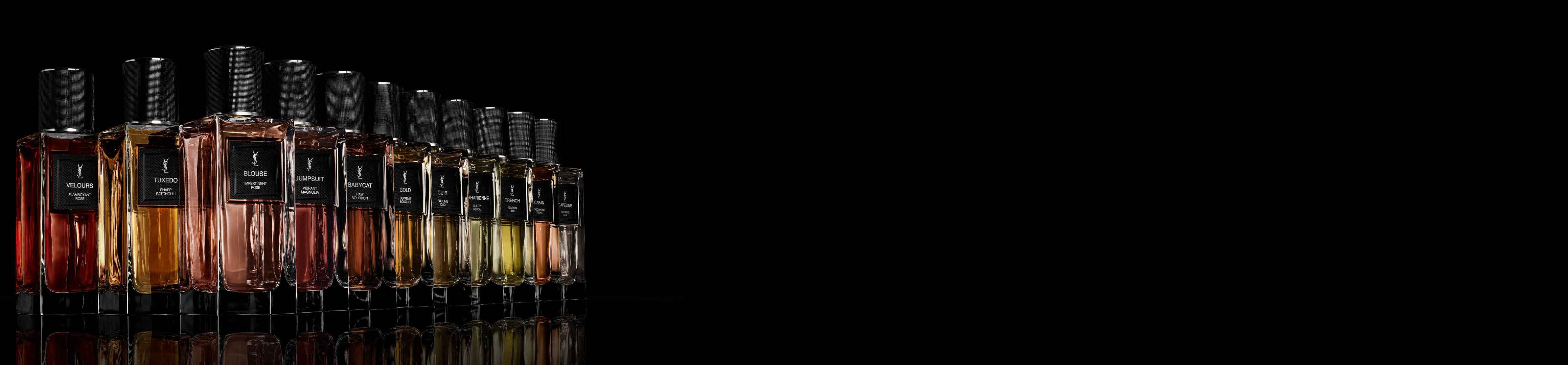 Een rij Yves Saint Laurent parfumflessen met verschillende vloeistofkleuren en zwarte getextureerde doppen, reflecterend op een donkere ondergrond tegen een zwarte achtergrond.