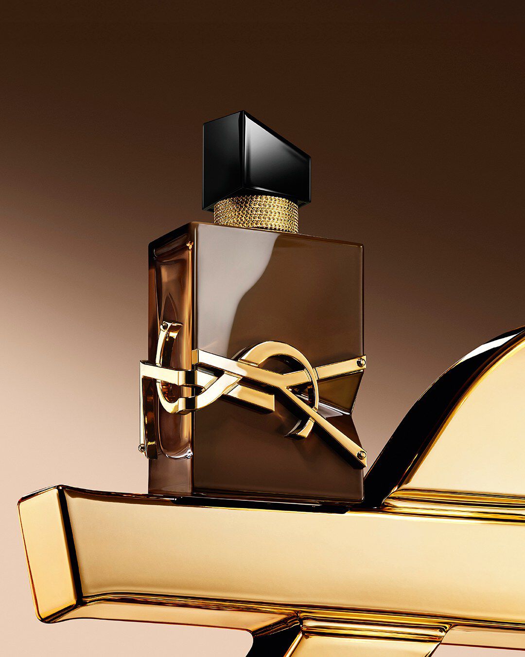Geglazuurde bruine Libre Santal Couture-flacon die het licht weerkaatst, geplaatst op een grote gouden YSL Cassandre.