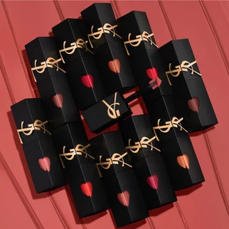 A collection of YSL lipstick cases arranged artfully on a coral background, featuring the brand's signature logo and heart-shaped openings displaying various shades of lipstick inside.