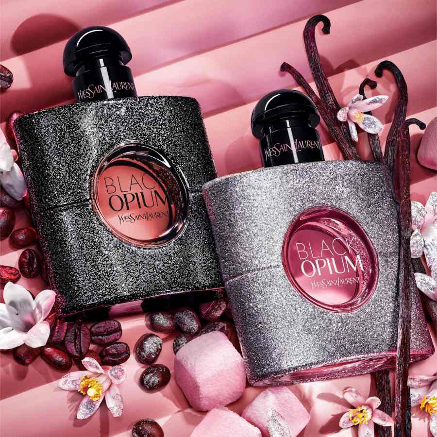 Twee YSL Black Opium-flacons op roze achtergrond met bloemen en koffiebonen