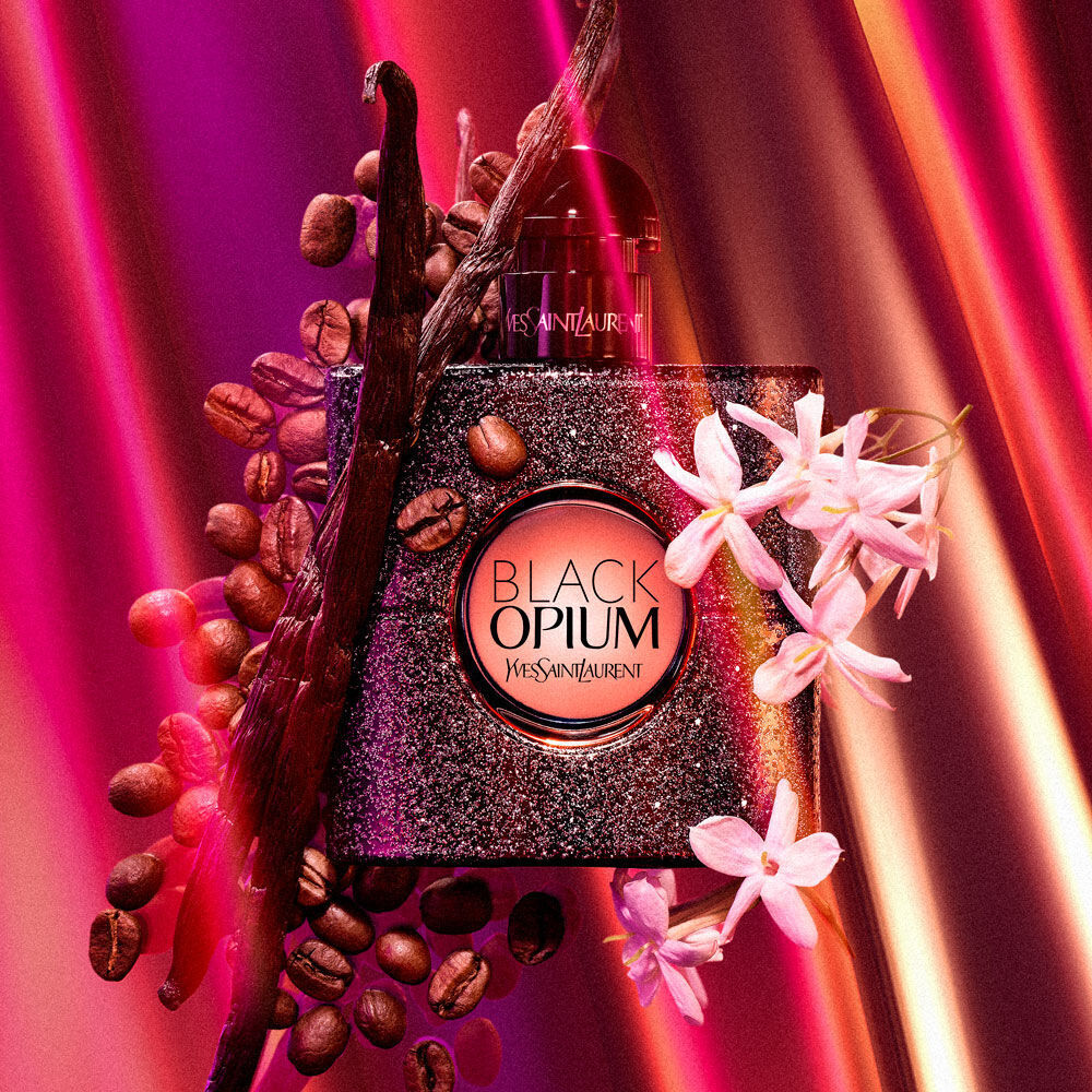 A stylish perfume bottle of "Black Opium" by Yves Saint Laurent surrounded by coffee beans and flowers, set against a vibrant, colorful background.