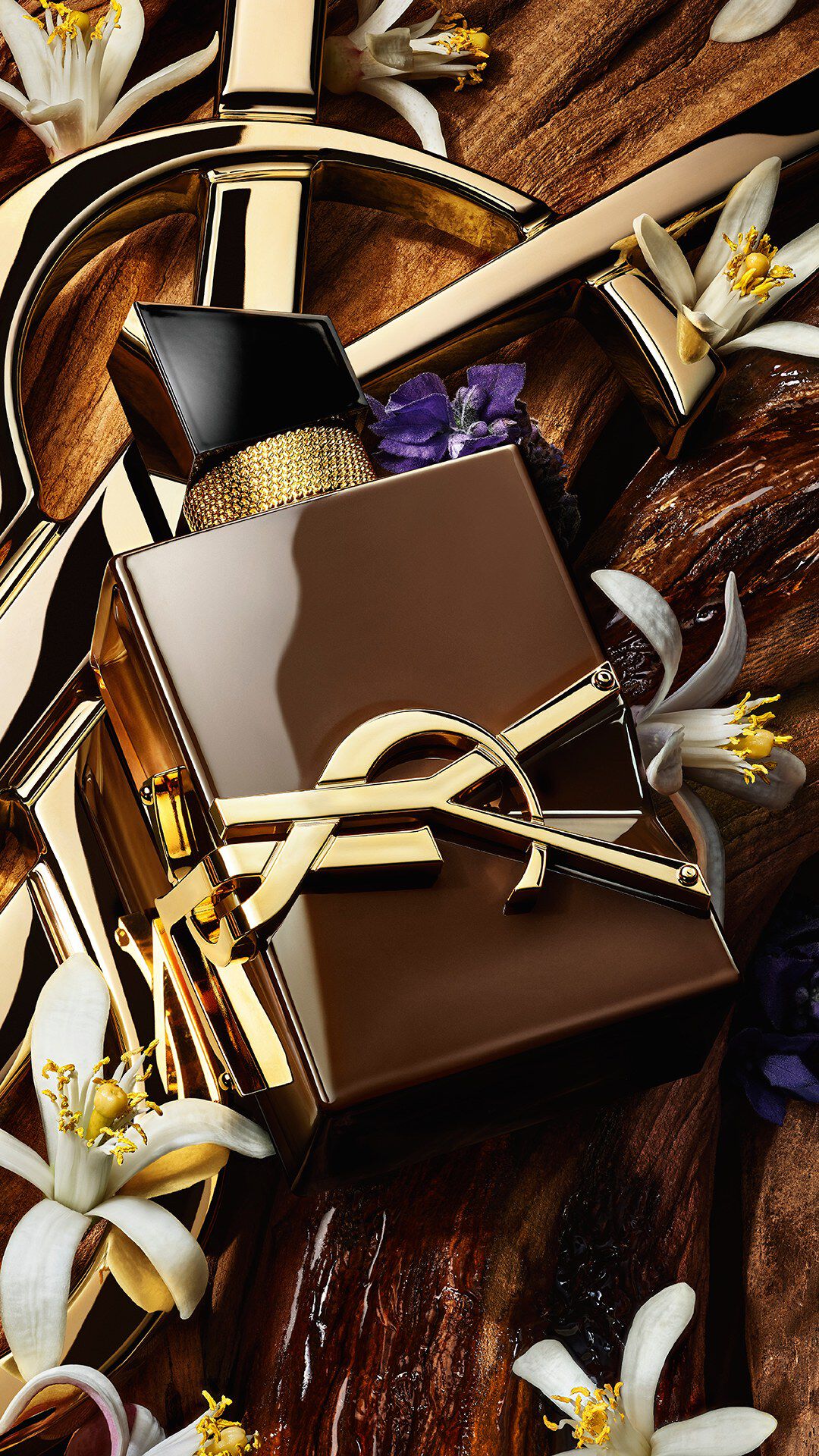Libre Santal Couture bottle on raw sandalwood bark with a golden YSL Cassandre in the background.