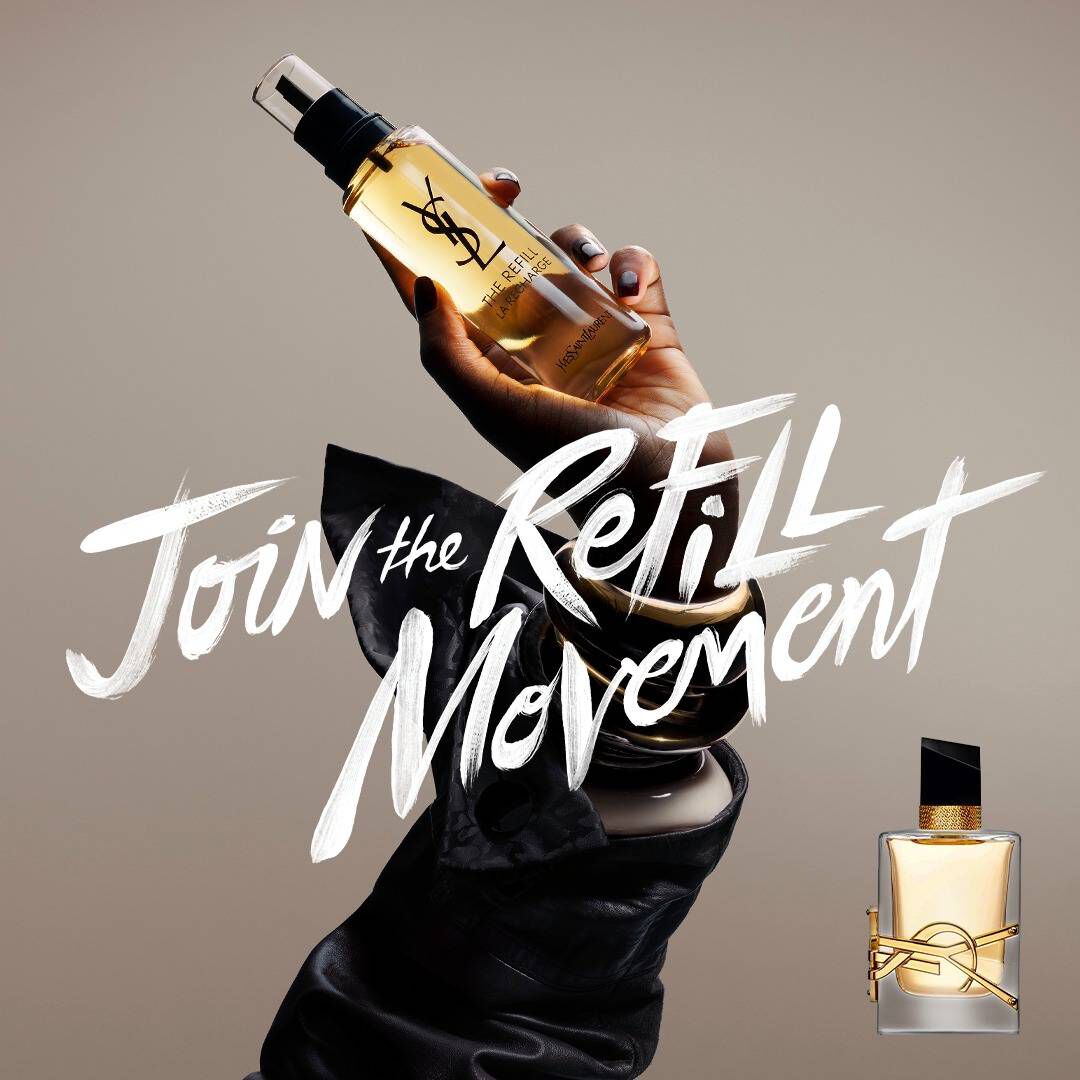 A hand holding a gold refill bottle against a neutral background. To the left, white brush-style text reads "Join the REFILL Movement," and to the right, a classic YSL Libre glass fragrance bottle with its signature gold logo is displayed.