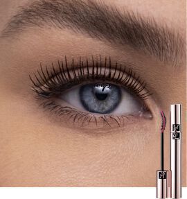 Close-up of a woman's eye showing long, defined eyelashes, with a mascara tube and wand positioned beside it.