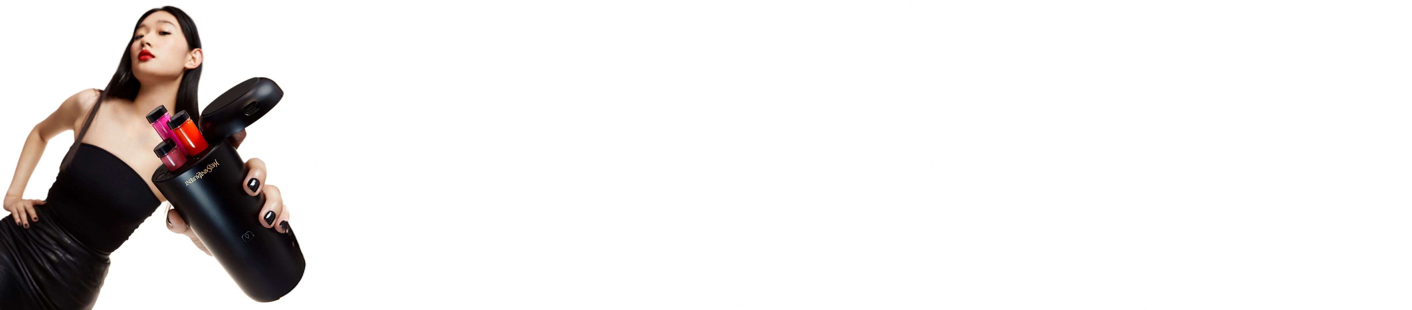 Een vrouw met rode lippenstift houdt een zwart Yves Saint Laurent schoonheidsapparaat vast met kleurrijke cosmetische inzetstukken.