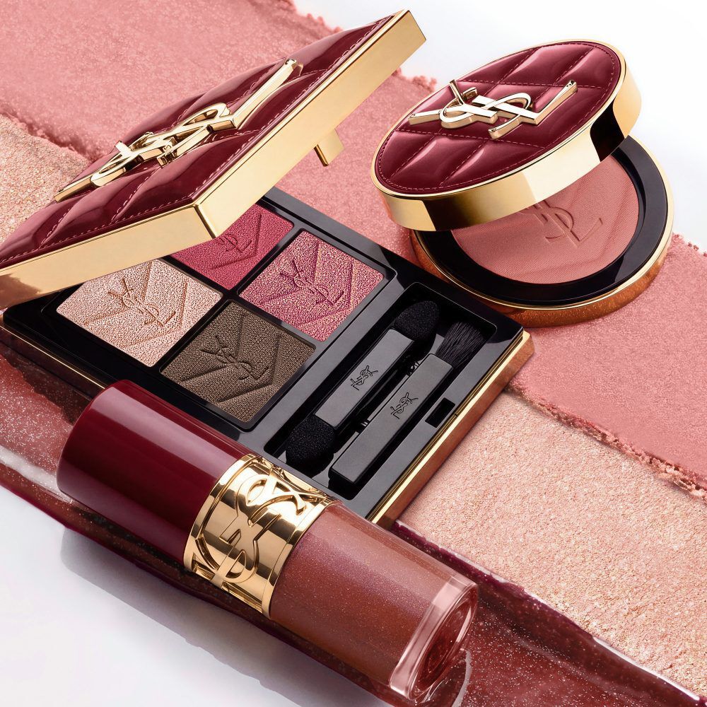Model in een zwart pak en een glamoureuze look, gezeten in een feestelijke kaarsverlichte setting met YSL cadeauverpakkingen.