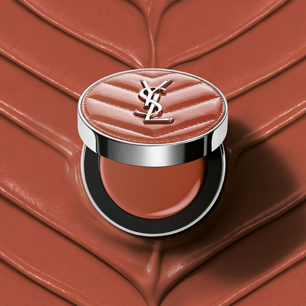 Een open YSL Make Me Blush Lifted Glow Cream Blush compact in tint #44 Nude Lavalliere op een bijpassende roze textuurcreme achtergrond.