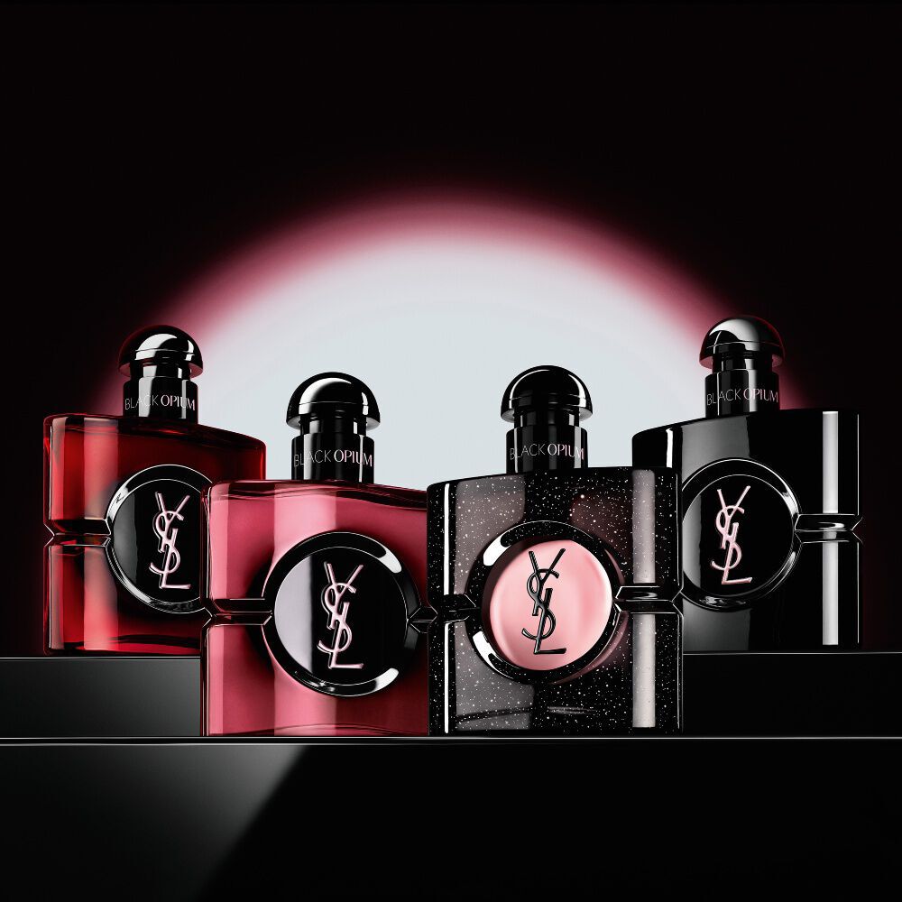Vier verschillende Black Opium-parfumflacons op een donkere, reflecterende ondergrond, naast elkaar gepresenteerd.