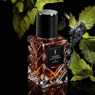 YSL LVDP Tuxedo Extrait de Parfum fles, omlijst door weelderige groene patchoulibladeren en tere paarse bloemen op zwart.
