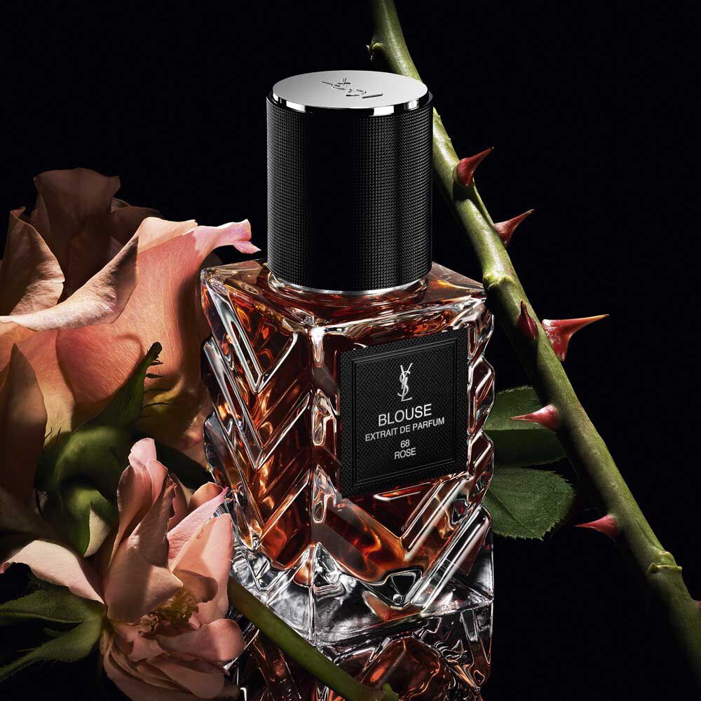 Driekwart aanzicht van YSL LVDP Blouse Extrait de Parfum fles, met roze rozen en doornige stengels op een donkere achtergrond.