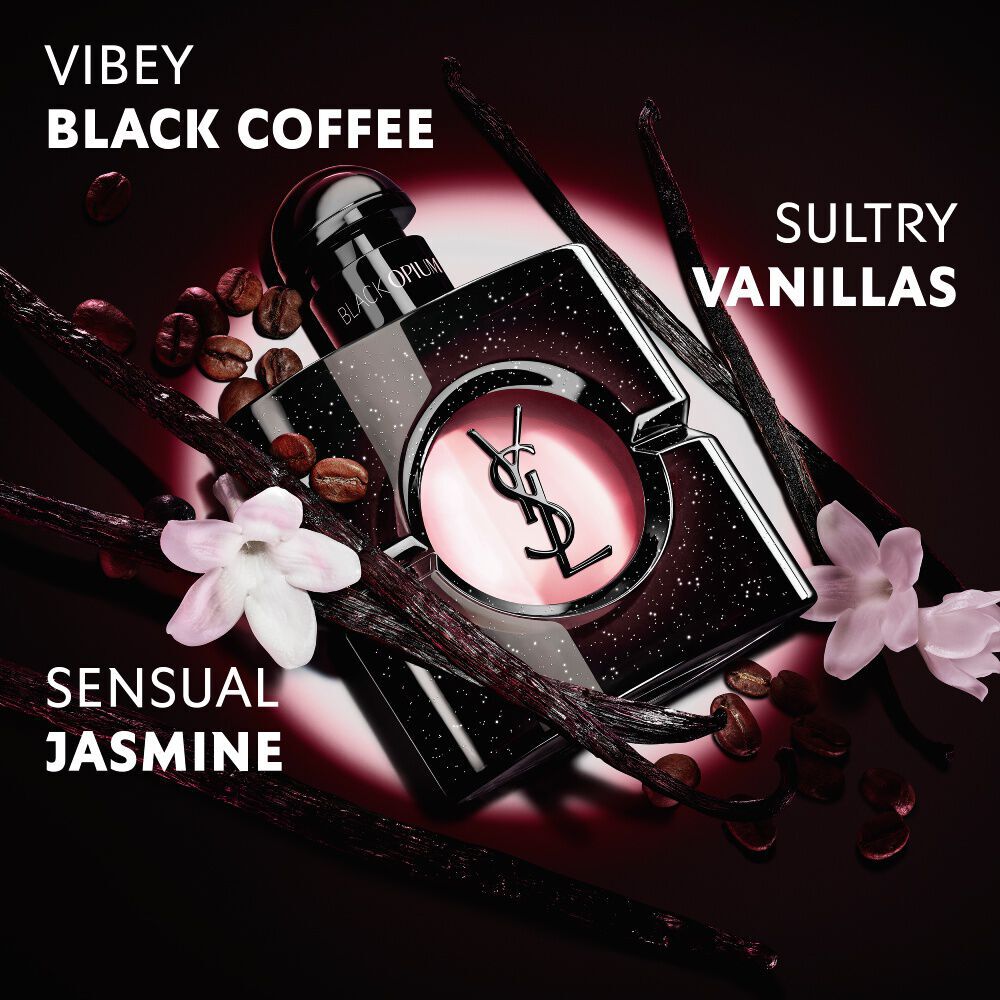 Close-up van gebrande koffiebonen, vanillepeulen en jasmijnbloemen, gerangschikt rond de iconische flacon Black Opium Eau de Parfum met de YSL Cassandre.
