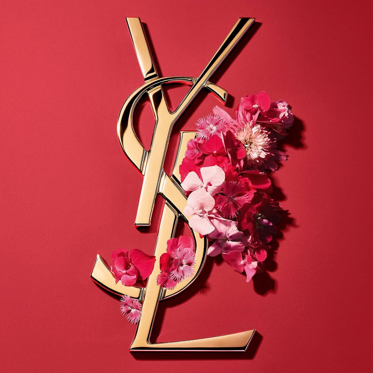Gouden YSL Cassandre-logo versierd met levendige roze lentebloemen, tegen een roze achtergrond.