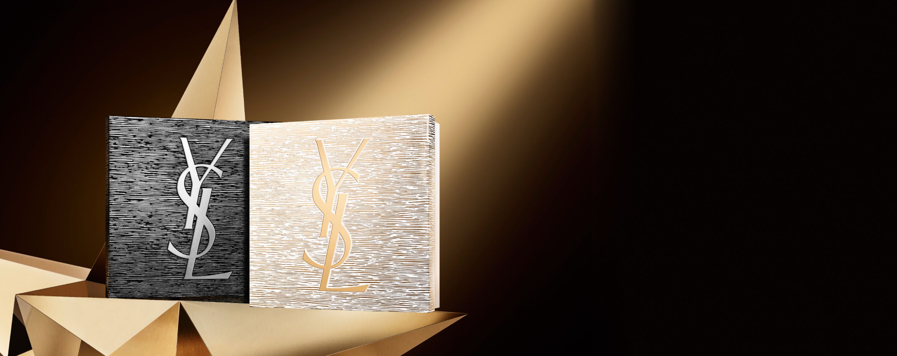 Twee elegante YSL Beauté-cadeausets voor de feestdagen, één zwart met een zilveren logo en één goudkleurig met een gouden logo, geplaatst op een geometrisch gouden oppervlak, wat een vleugje haute couture en glans geeft.