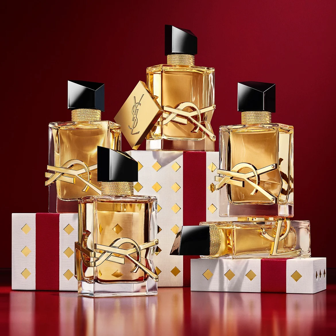 Multiple YSL LIBRE fragrance bottles layered over luxury gold-patterned Holiday gift packaging.