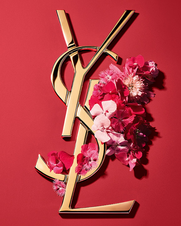 Gouden YSL Cassandre-logo versierd met levendige roze lentebloemen, tegen een roze achtergrond.