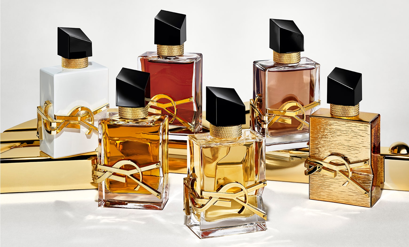 Zes YSL Libre-parfumflesjes staan ​​op een glanzend gouden oppervlak. De flesjes vertonen variaties in de kleur van de vloeistof en de afwerking, waaronder heldere, witte, roodachtige en bruine tinten, en een volledig gouden fles met textuur. Alle flesjes zijn voorzien van de iconische gouden YSL-letters en een schuine zwarte dop.




