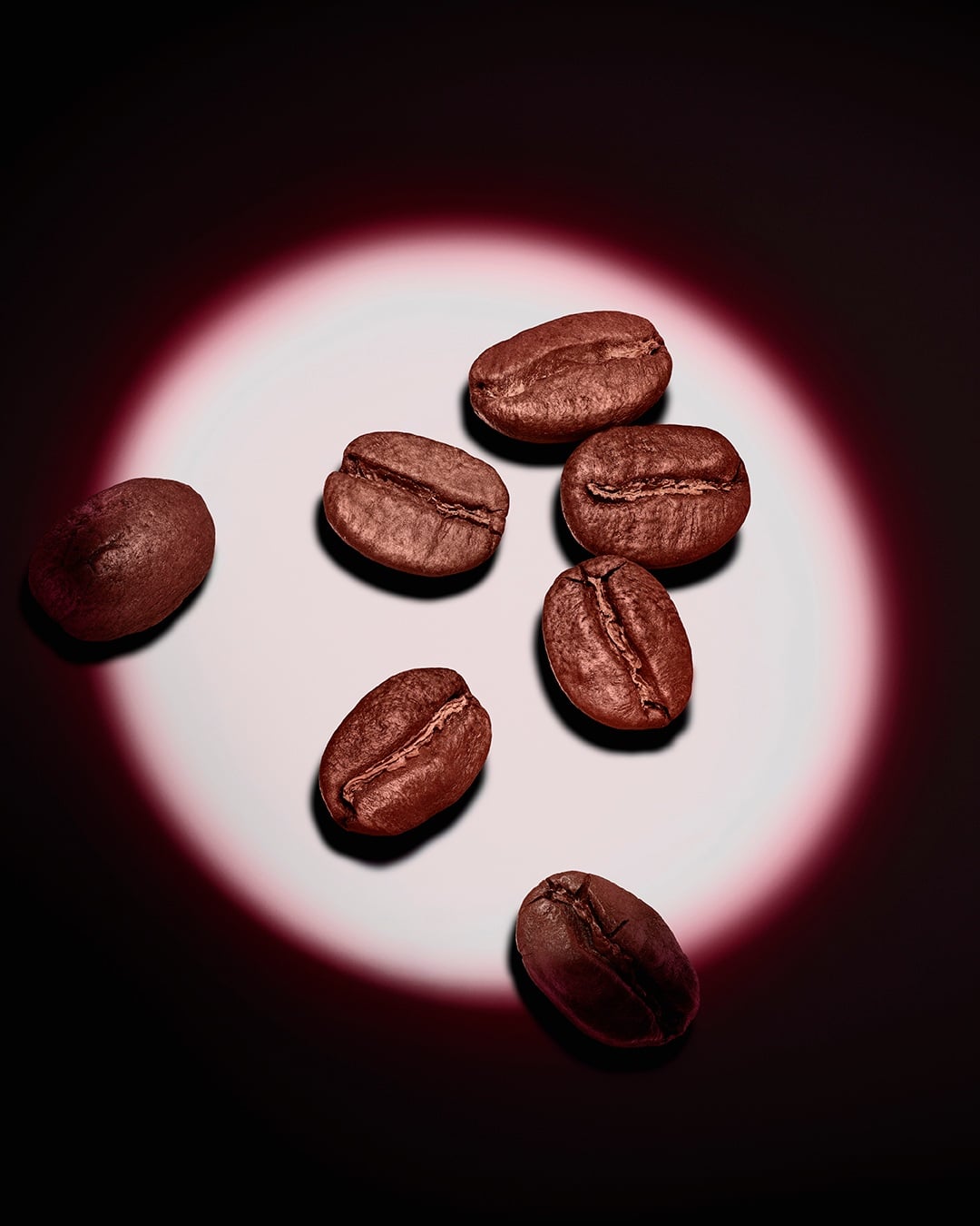 Een groep gebrande koffiebonen, uitgelicht door een roze ronde spot tegen een donkere achtergrond.