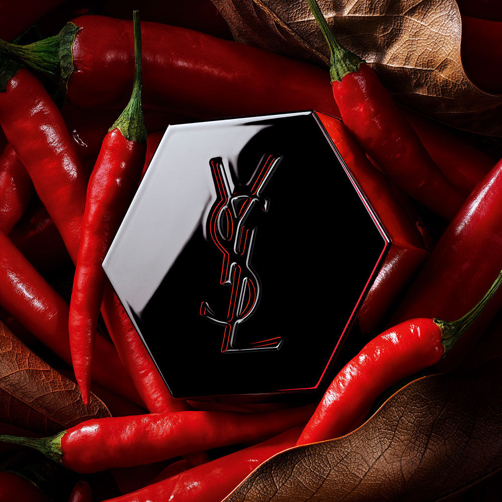 Zwarte zeshoekige YSL parfumdop met een rood omlijnd logo, omringd door rode chilipepers.