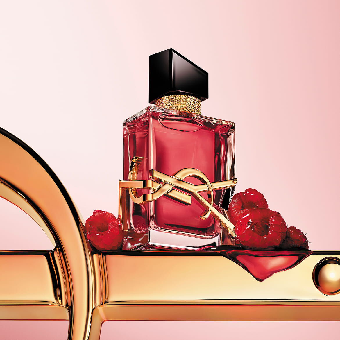 Rode YSL-parfumfles met gouden logo, op een gouden oppervlak met frambozen.