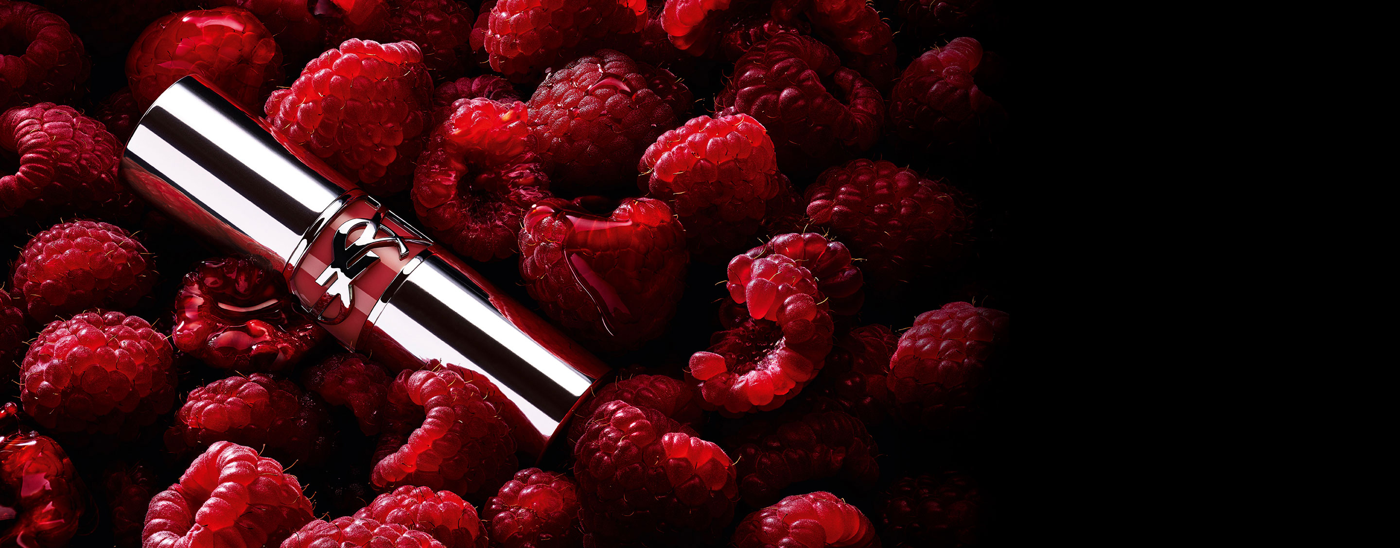YSL LOVESHINE Berry Crush lipstick, zilveren huls met bessenkleurig YSL-logo, genesteld tussen verse frambozen.