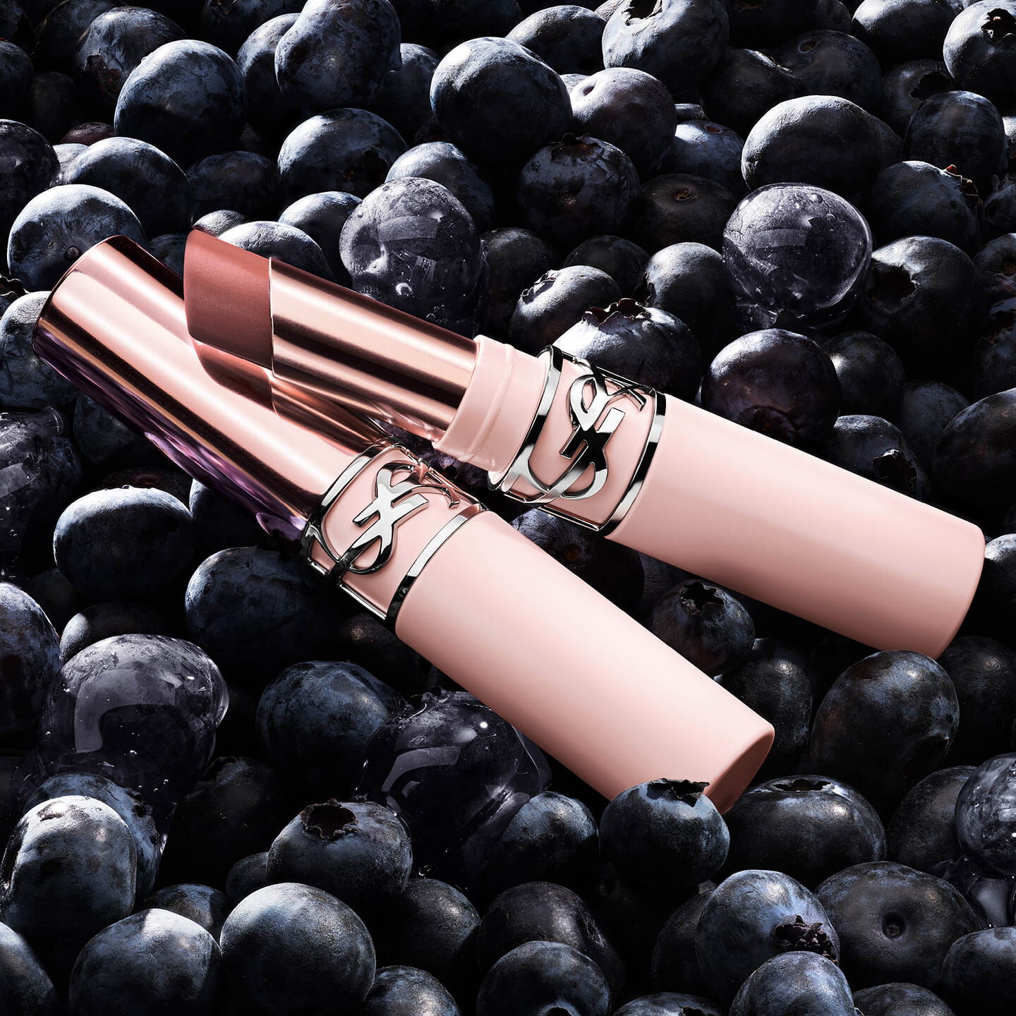 Two YSL LOVENUDE Lip Blusher products in Shade 7, nestled among blueberries, highlighting natural ingredients.