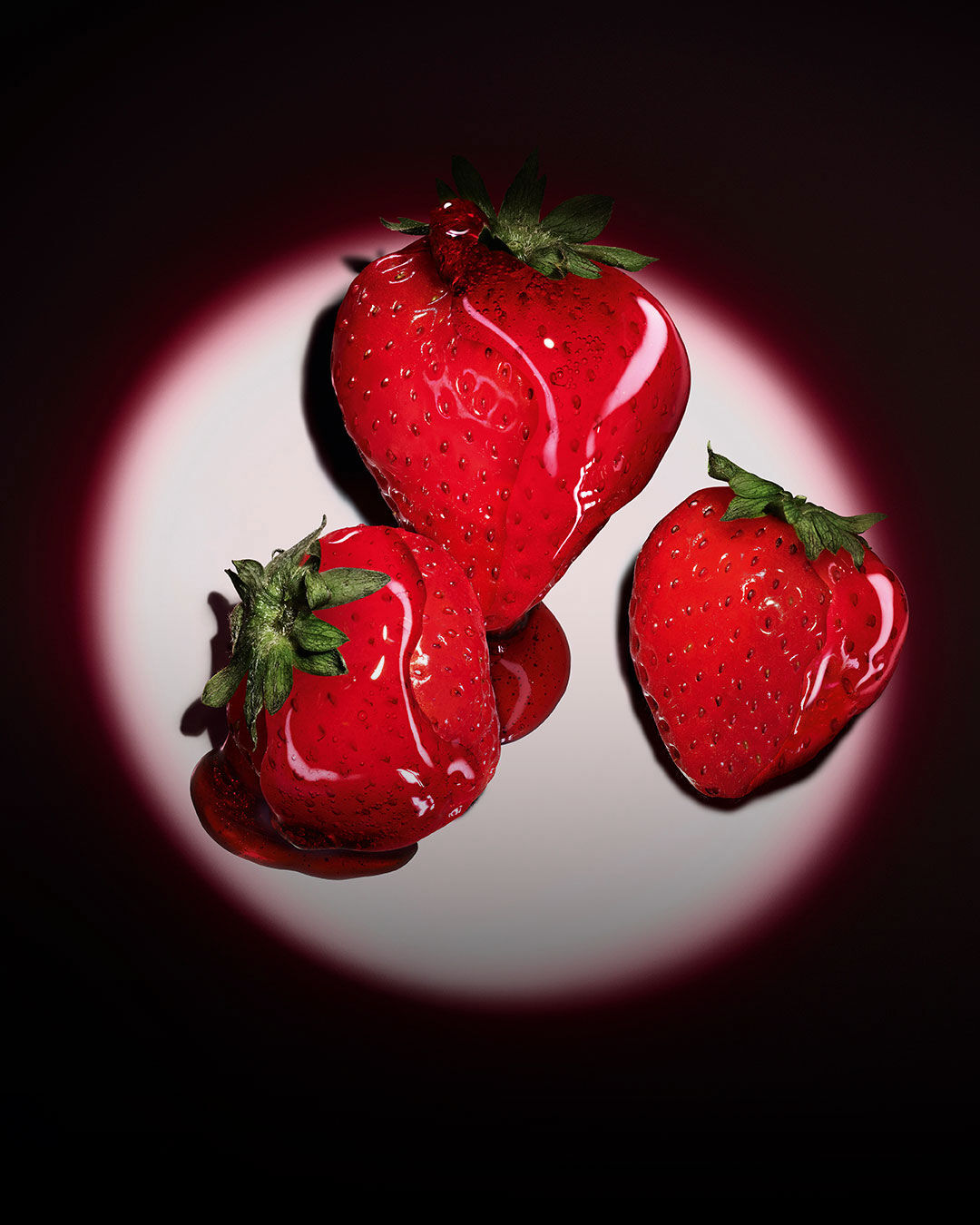 Drie verse rode aardbeien verlicht door een roze cirkelvormige spotlight op een donkere achtergrond.