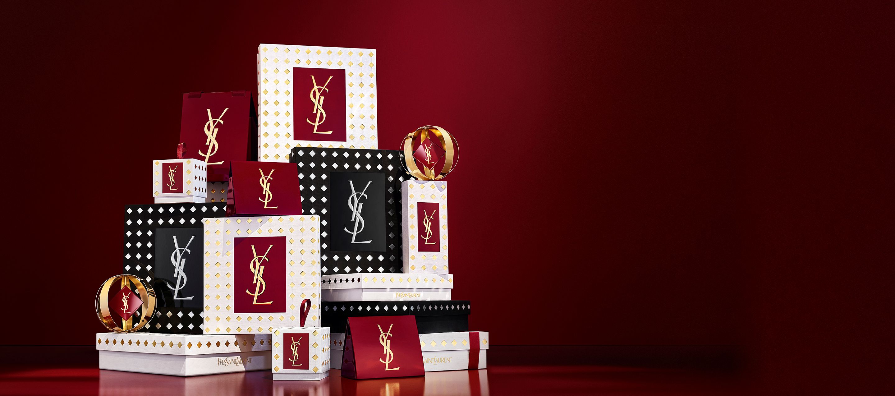 Drie modellen in elegante zwarte outfits houden YSL-cadeausets vast voor een feestelijk rood gordijn met vallende gouden confetti.