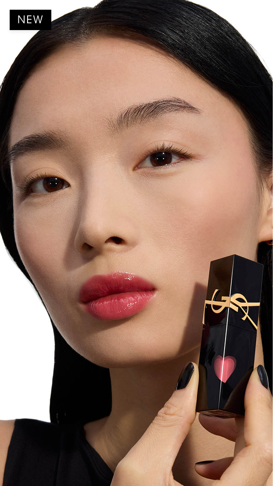 Light skin tone model with a glossy berry-pink lip look holding the black YSL THE INKS VINYL CREAM lip stain bottle with its shiny red heart.