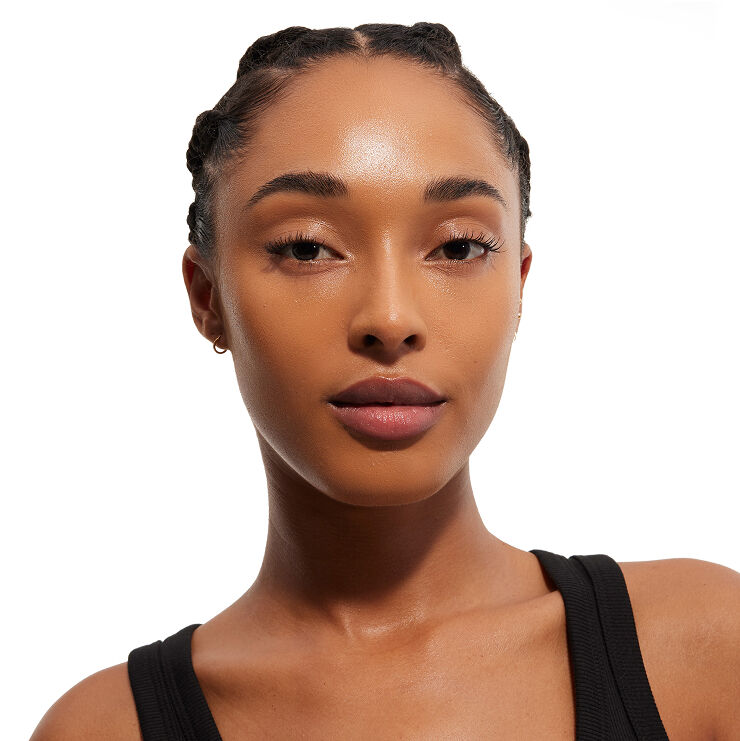 Hoofdshot van een vrouw met gevlochten haar en een vlekkeloze huid, gekleed in een zwarte top, die rechtstreeks naar de kijker kijkt en make-up op haar gezicht toont.