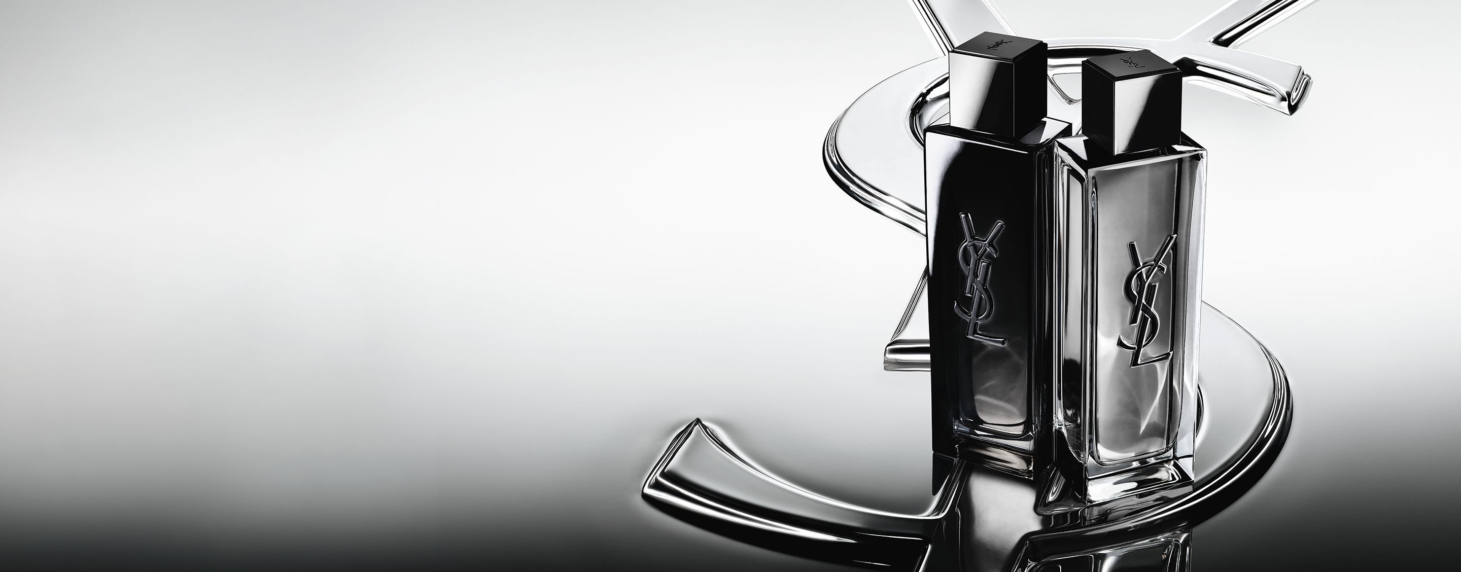 De flacons van MYSLF Eau de Parfum en MYSLF Eau de Toilette Intense staan naast elkaar op een groot YSL Cassandre-logo met een spiegelend effect.