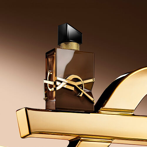 Geglazuurde bruine Libre Santal Couture-flacon die het licht weerkaatst, geplaatst op een grote gouden YSL Cassandre.