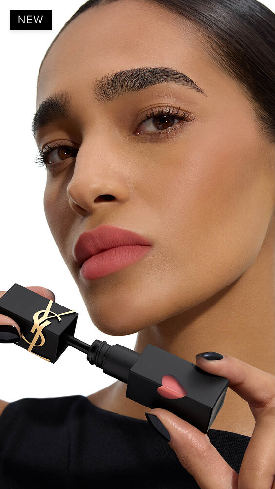 Model met een diep-middelmatige huidskleur en een soft-focus matte lippenlook, die de applicator van YSL THE INKS BLUR lippenvlek naast haar kin houdt.