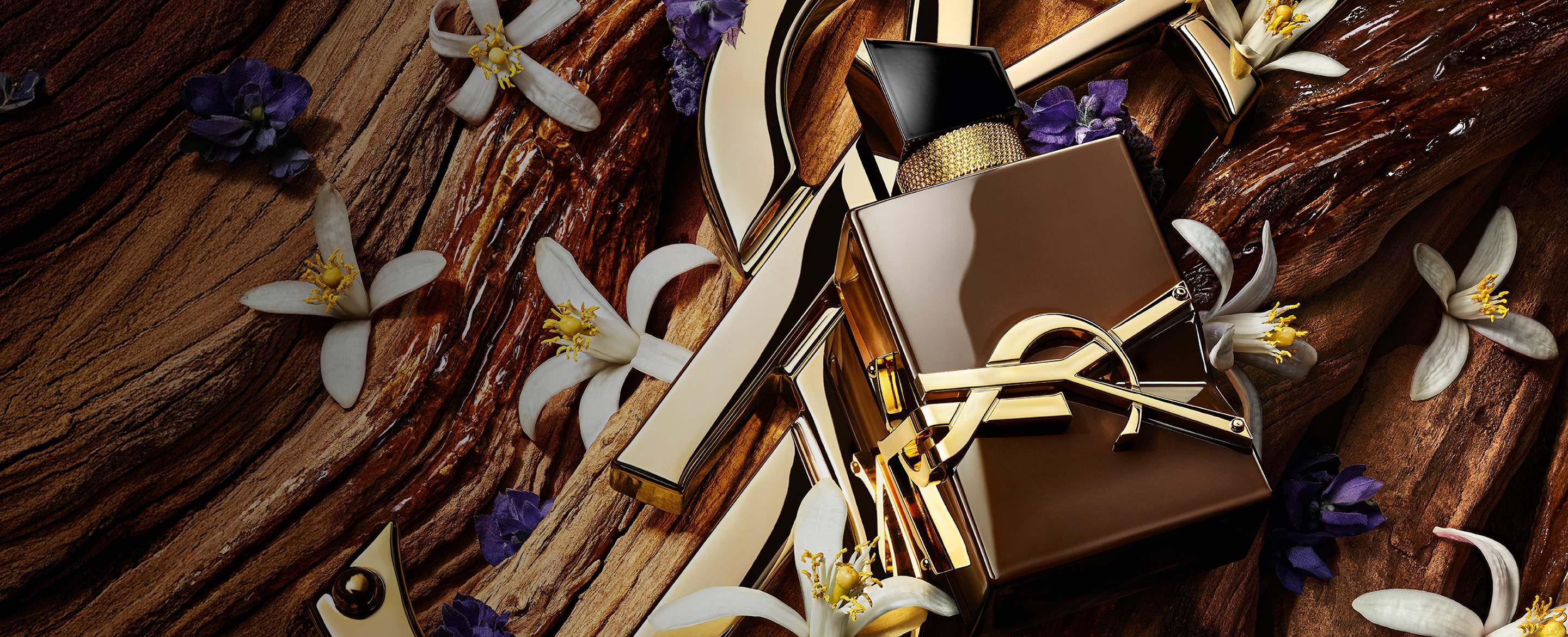 Geglazuurde bruine Libre Santal Couture-flacon die het licht weerkaatst, geplaatst op een grote gouden YSL Cassandre.